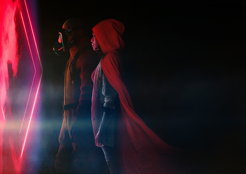 A photograph of 2 people in profile looking towards a red, diamond shaped light. The person to the left is wearing a gas mask, the person to the right is wearing a red scarf. The red light is the only light source and the photo is dark and moody.