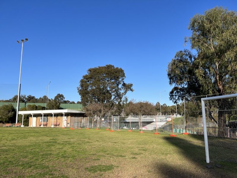 A view from a sports field towards a small building and a lot of temporary construction fencing beside it.