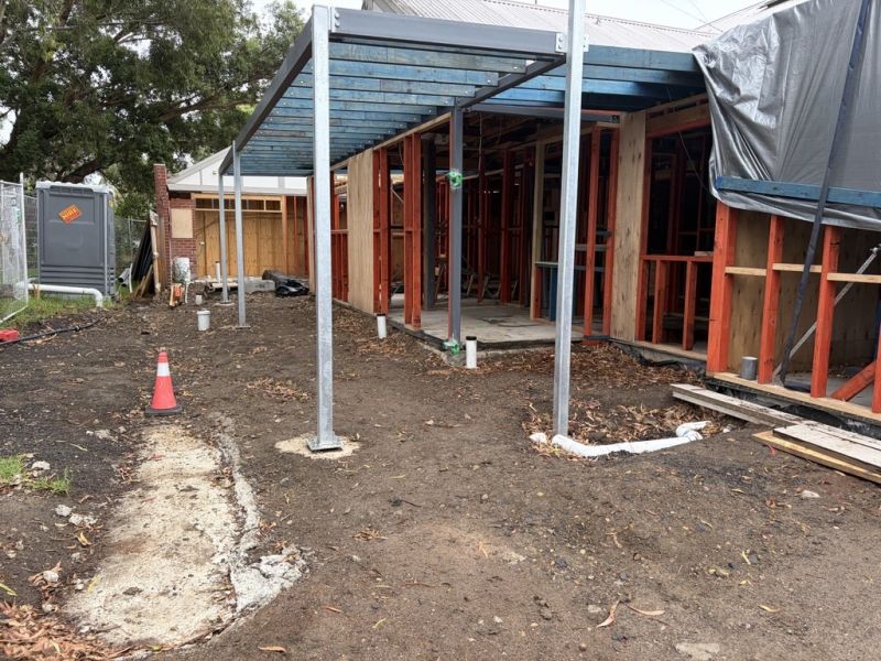 A small building under construction. The side is open and we can see exposed beams and the foundations for an awning.