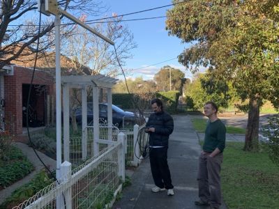 Two people standing on a suburban footpath looking up at the boom mounted charger. One of them is holding an extension lead.