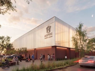 A computer generated impression of a large rectangular building around 3 storeys high. There is an older building behind it and a car park in front. The building is peach coloured tiles and concrete with a corrugated iron top storey.