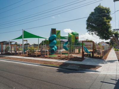 A view of a new playground from across a road. There is brightly coloured equipment and a big shade sail