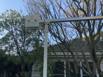 A close up view of the pole and boom hinge. The poles are white and narrow. In the background is a house and tree. 