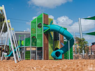 A brightly coloured climbing tower in a new playground. There is a long tube slide that winds around the frame.