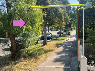 A view of a suburban footpath. There is a pole in the front yard of the house in view. A boom is opened out from the pole across the footpath with an extension lead coming down from the boom.