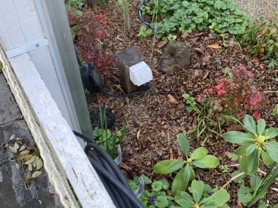 A close up view of the pole at ground level. It is installed in a garden bed with an outdoor electrical outlet next to it.